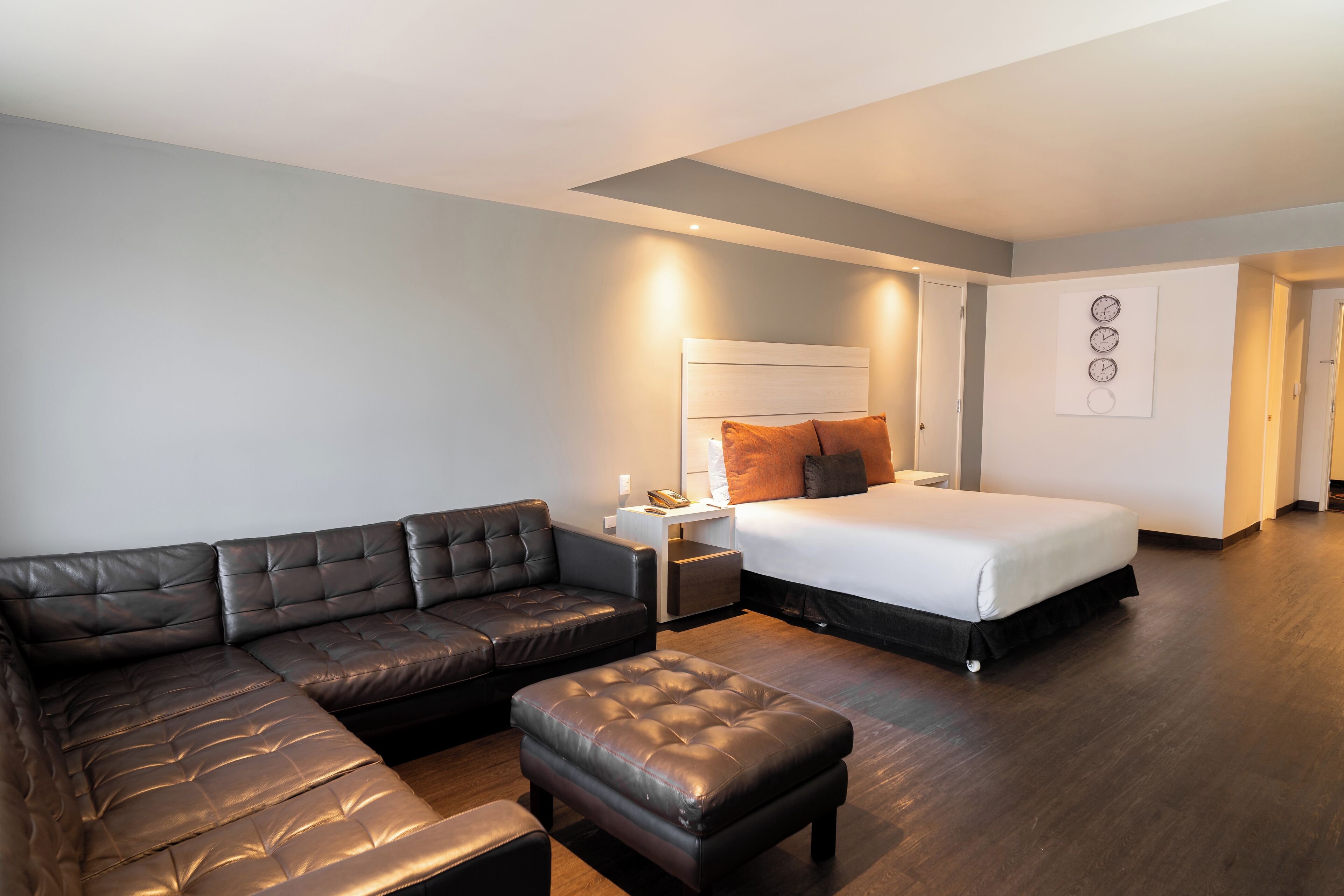 A modern hotel room with a sectional sofa, a bed, and a nightstand.