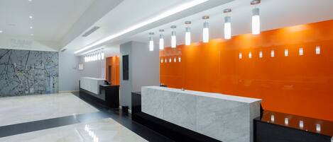 Uma área de recepção moderna com balcão de mármore, paredes com detalhes em laranja e iluminação pendente.