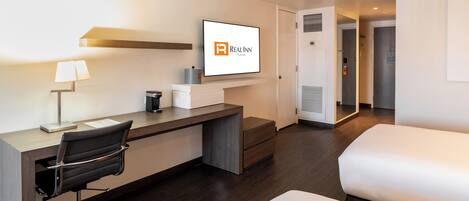 Habitación de hotel con escritorio, silla, cama y un televisor mostrando el logotipo de Real Inn.