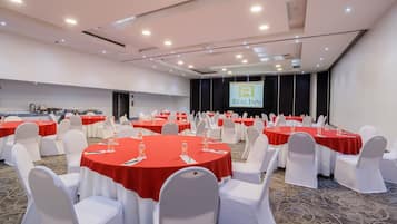 A conference room with multiple round tables, white chairs, and red tablecloths.