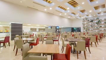 A spacious indoor dining area with multiple tables and chairs, a counter with a display, and shelves with plants.