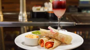 Un plato con dos wraps, un cuenco pequeño de salsa y un vaso de bebida roja sobre una mesa.