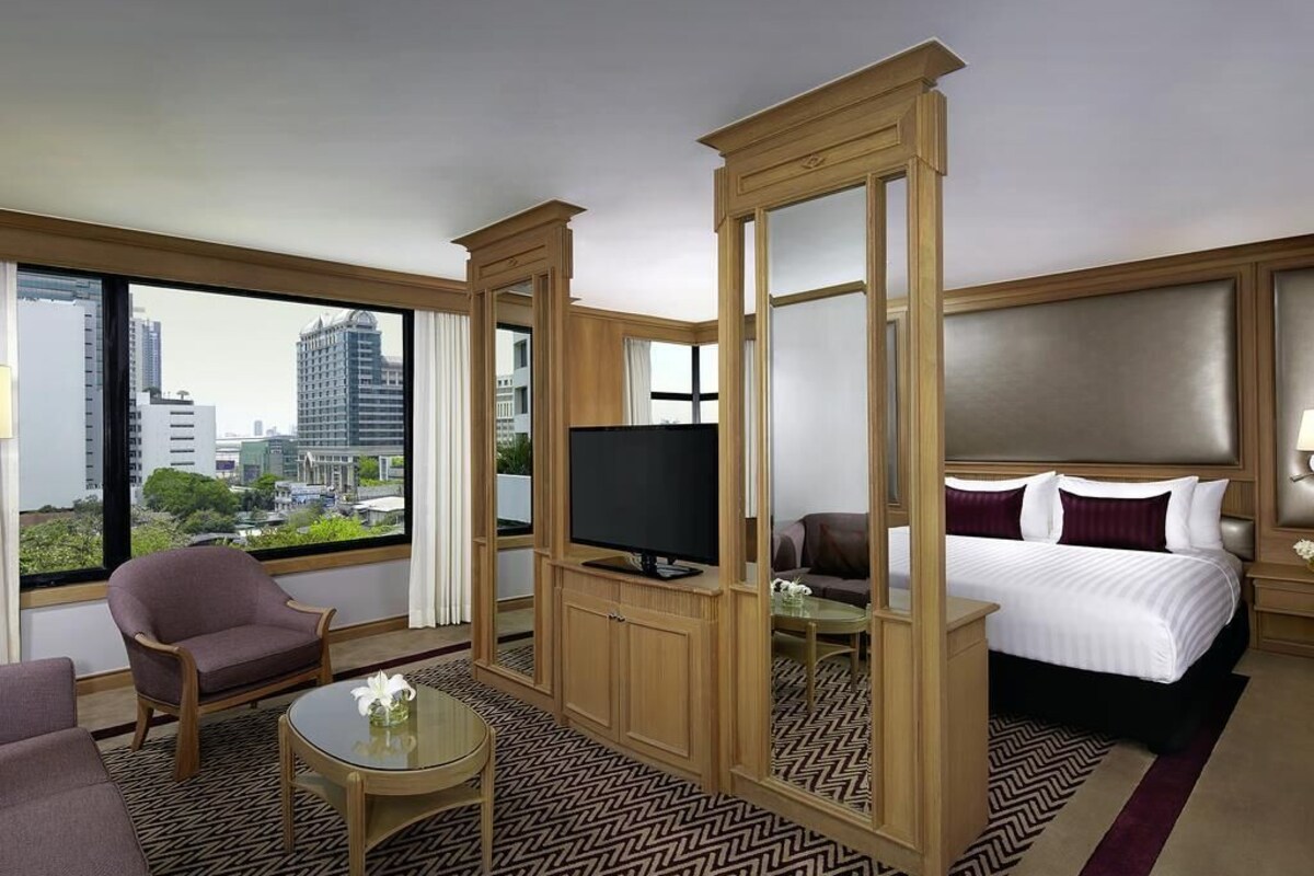 A hotel room with a large window, a bed, a TV, a sofa, and a coffee table.