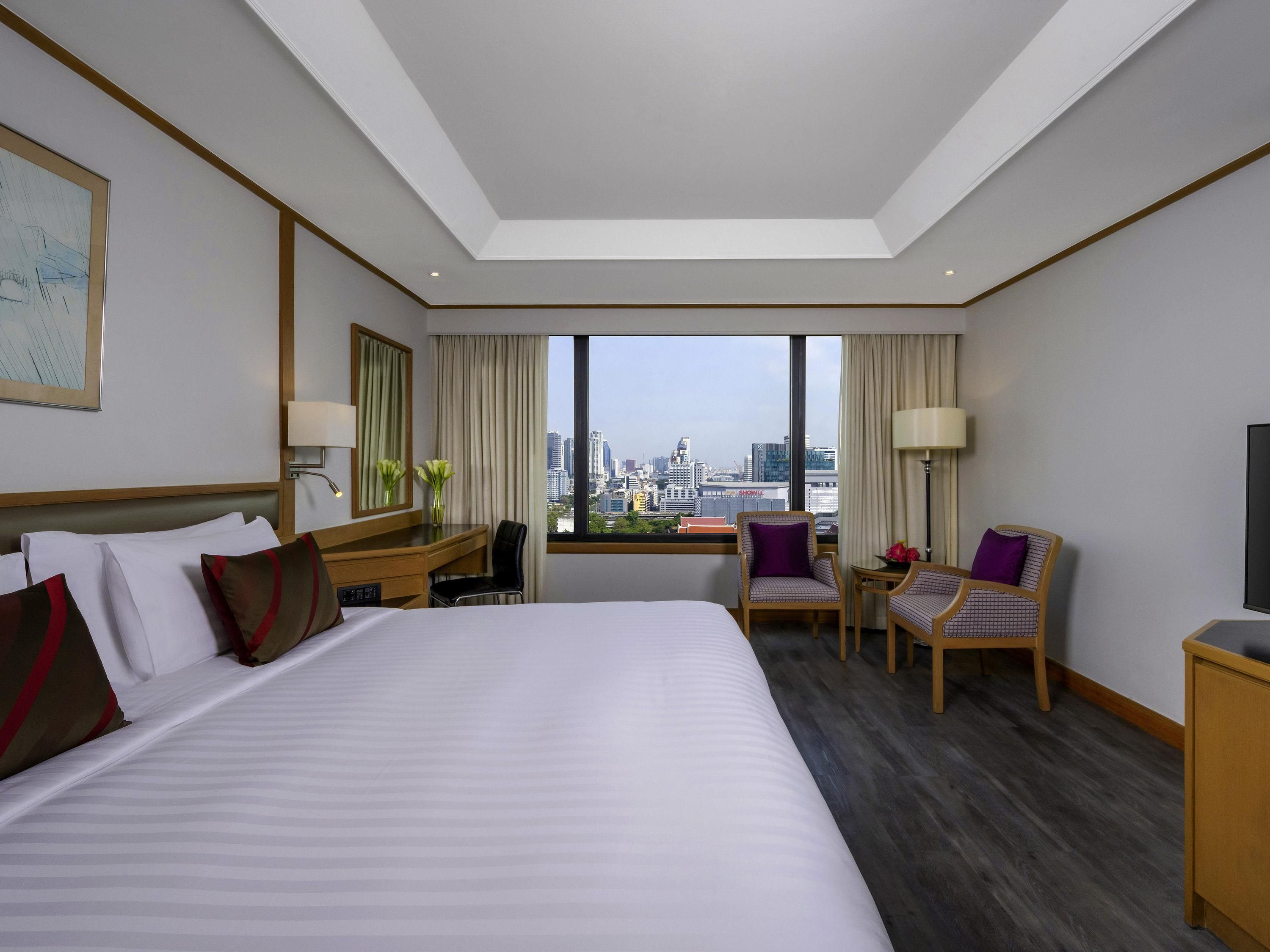 A hotel room with a large bed, a desk, two chairs, a TV, and a city view.