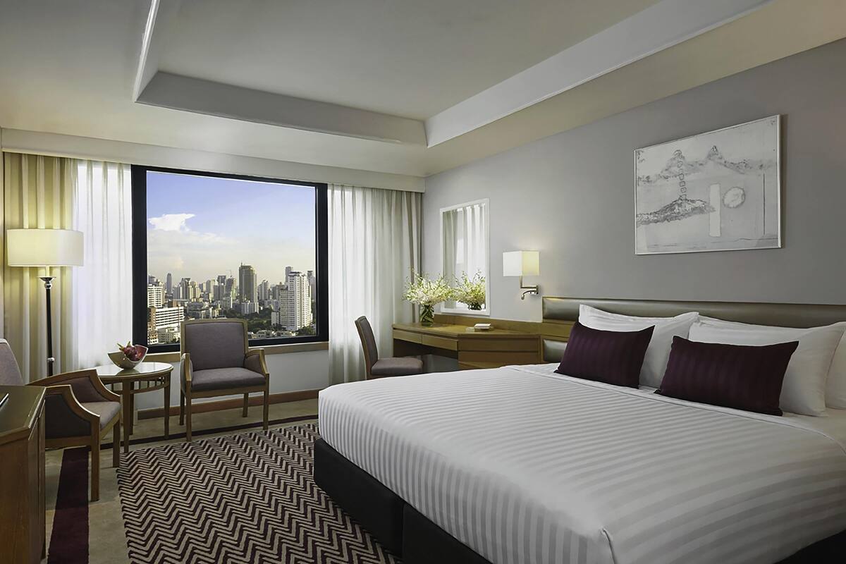 Une chambre d’hôtel avec un grand lit, un bureau, une chaise, une fenêtre donnant sur la ville et un tableau au mur.