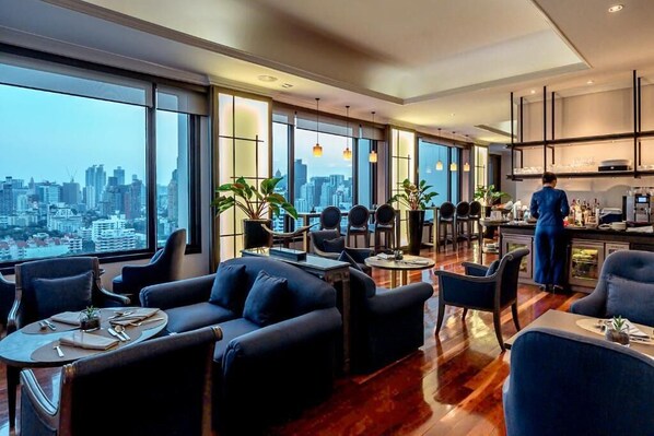 A modern hotel room with a city view, a dining area, and a kitchen.