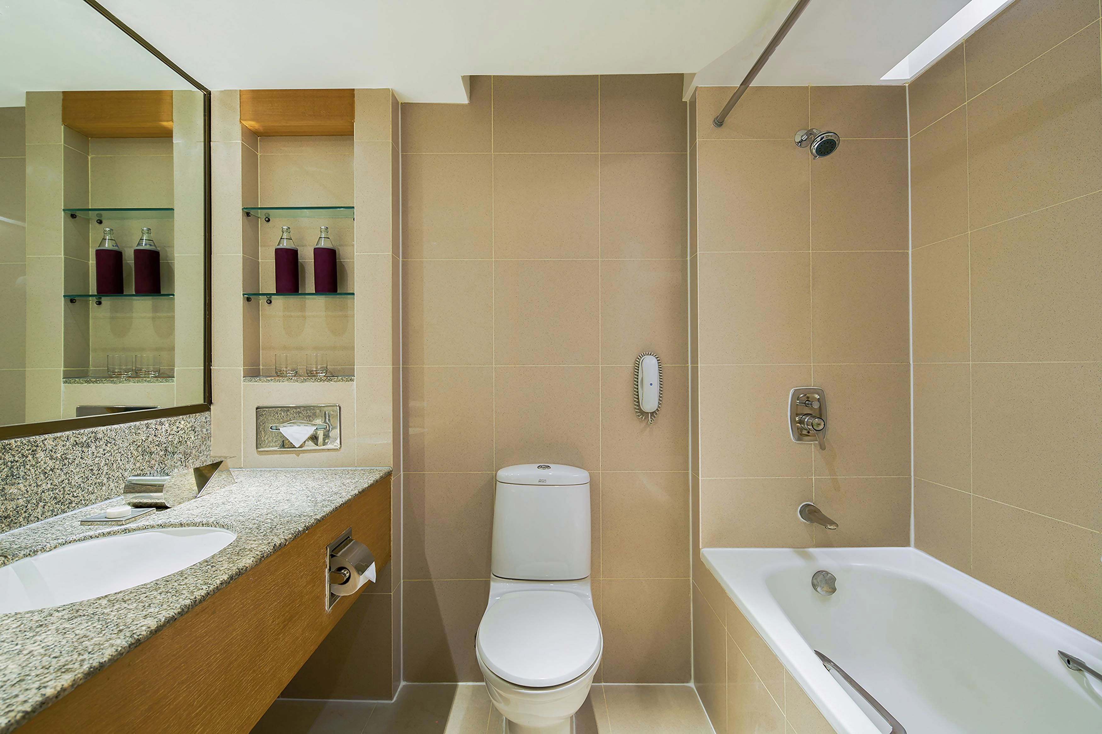 A bathroom with a toilet, sink, and bathtub. There are shelves with bottles and a mirror above the sink.