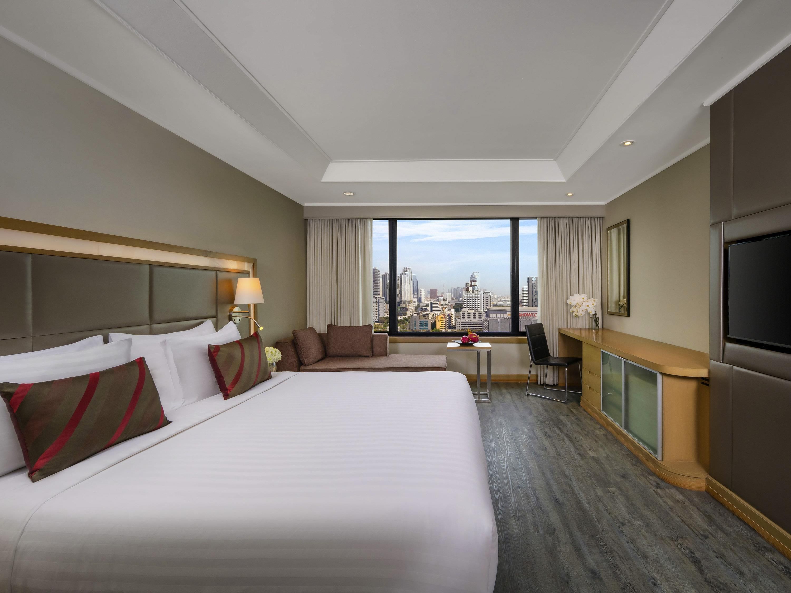 A hotel room with a large bed, a desk, a chair, a TV, and a city view.