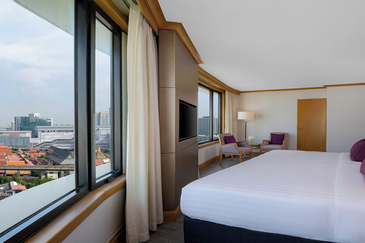 A hotel room with a large bed, a TV, a desk, and a chair.