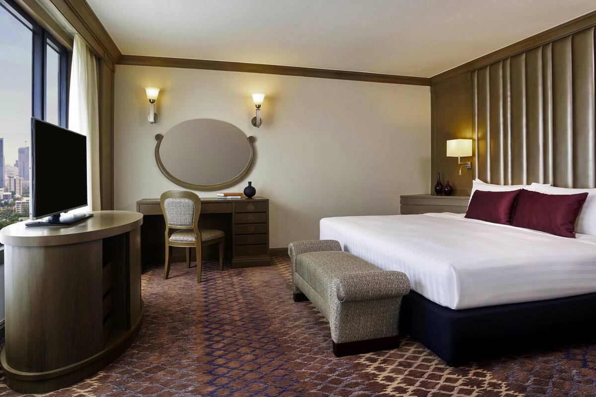 Une chambre d’hôtel comprenant un lit, un bureau avec une chaise, un miroir rond et un téléviseur.