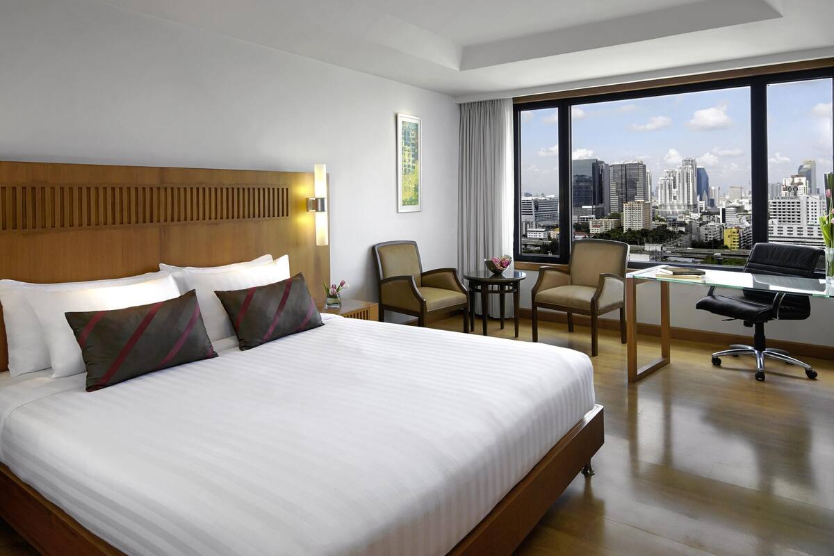Une chambre d’hôtel avec un grand lit, un bureau, deux chaises et une vue sur le paysage urbain.