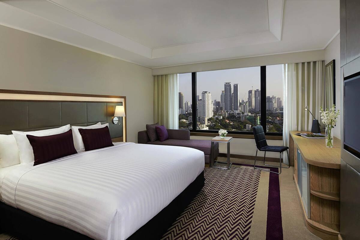 Une chambre d’hôtel avec un grand lit, un bureau, une chaise, une télévision et une vue sur le paysage urbain.