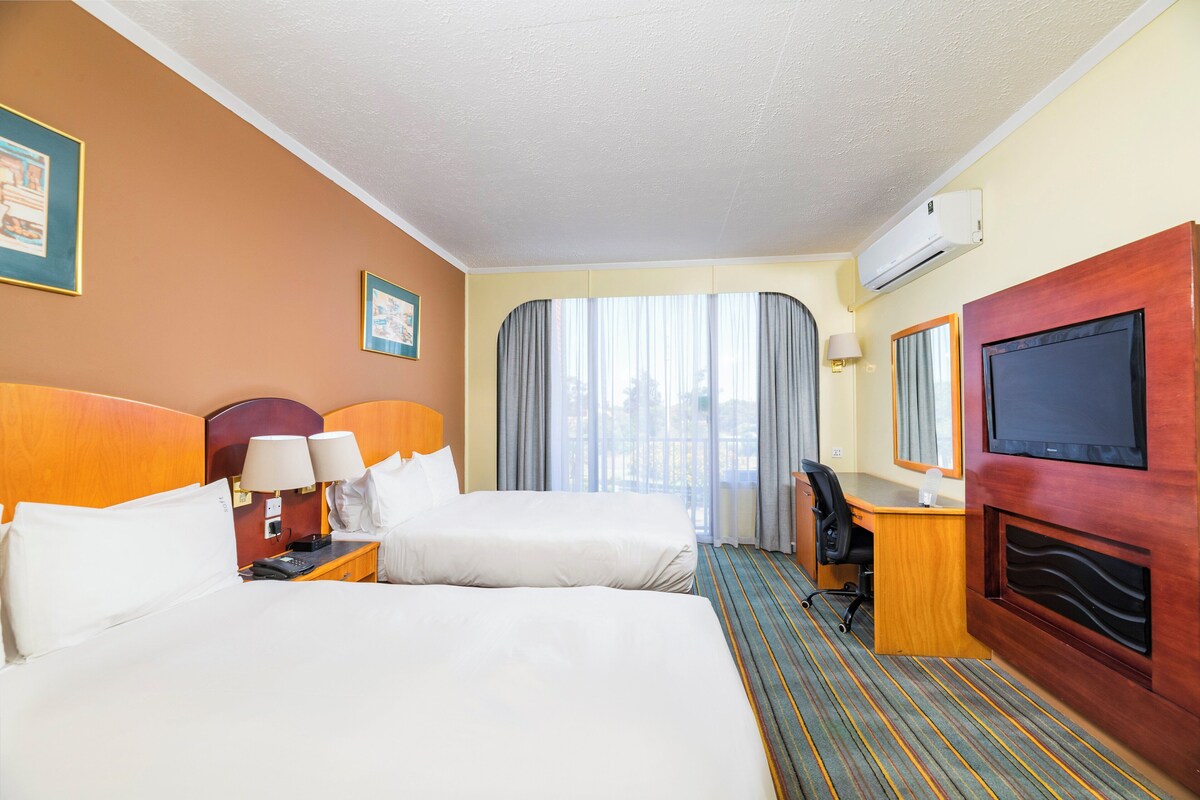 A hotel room with two beds, a desk, a chair, a TV, and a window with curtains.