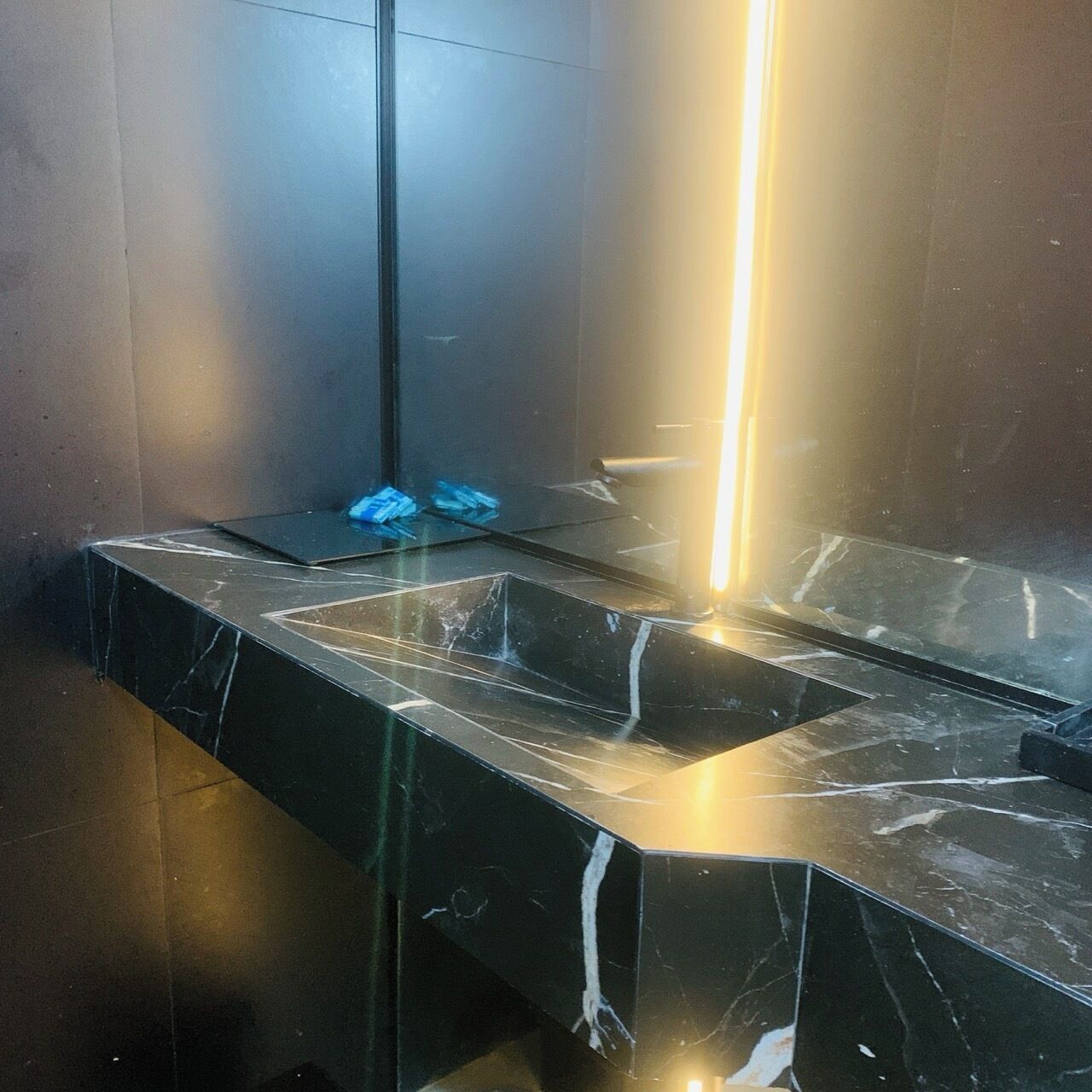 A modern bathroom with a black marble sink and a vertical light fixture.