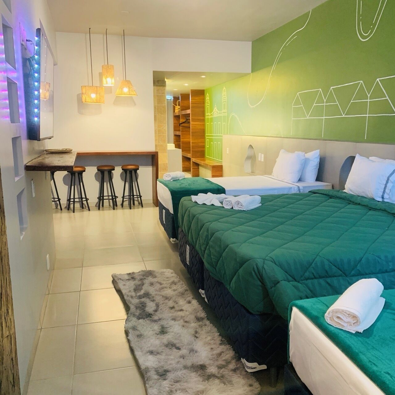 Hotelkamer met een groene wand, een bed met witte kussens, een bureau met krukken en een klein zitgedeelte.