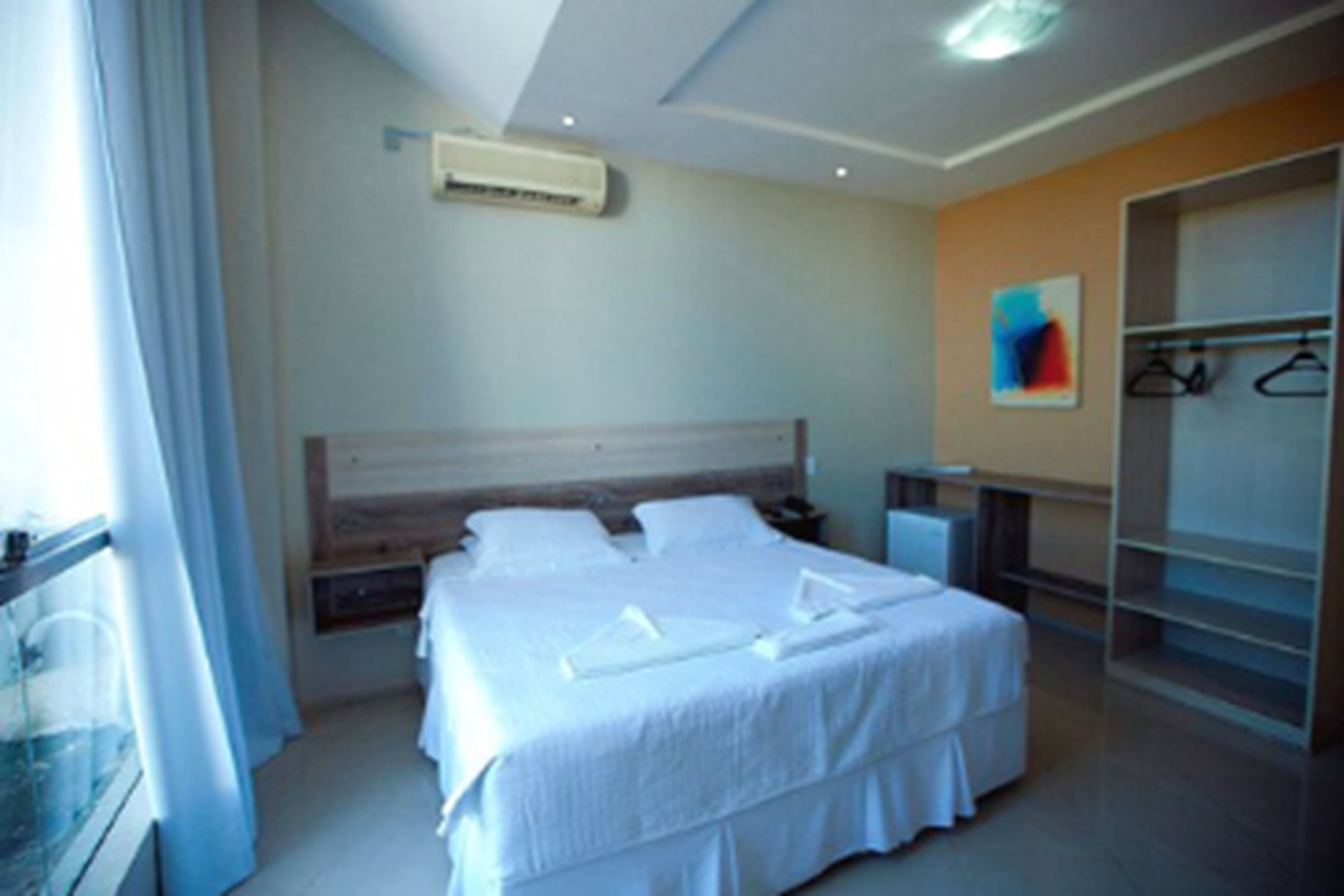 A hotel room with a large bed, a wardrobe, and a window with curtains.