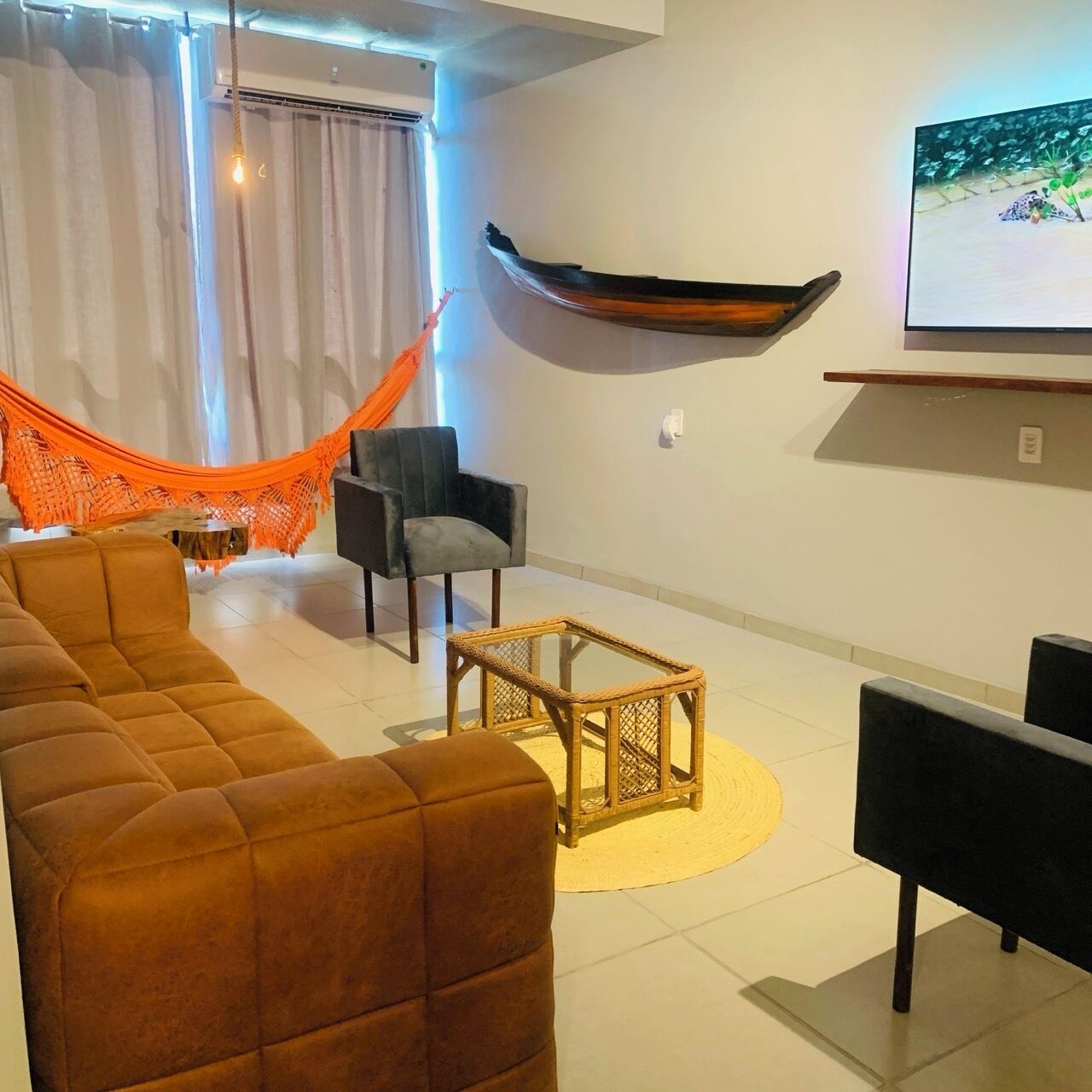 A modern living room with a large sofa, a small coffee table, a hammock, and a mounted television.