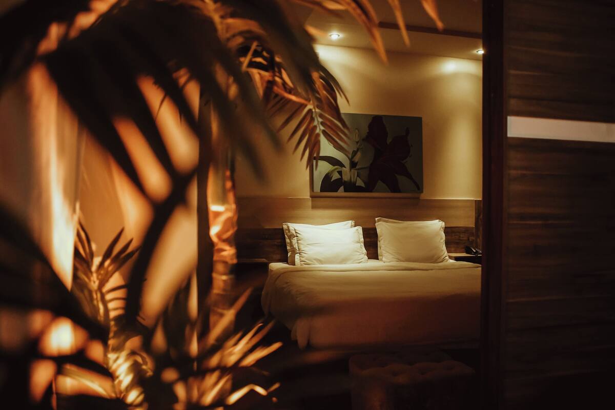 A bedroom with a bed, pillows, a nightstand, and a painting on the wall.