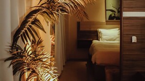 A hotel room with a bed, a nightstand, a bedside table, and a potted plant. - Barrudada Tropical Hotel (Santarém)