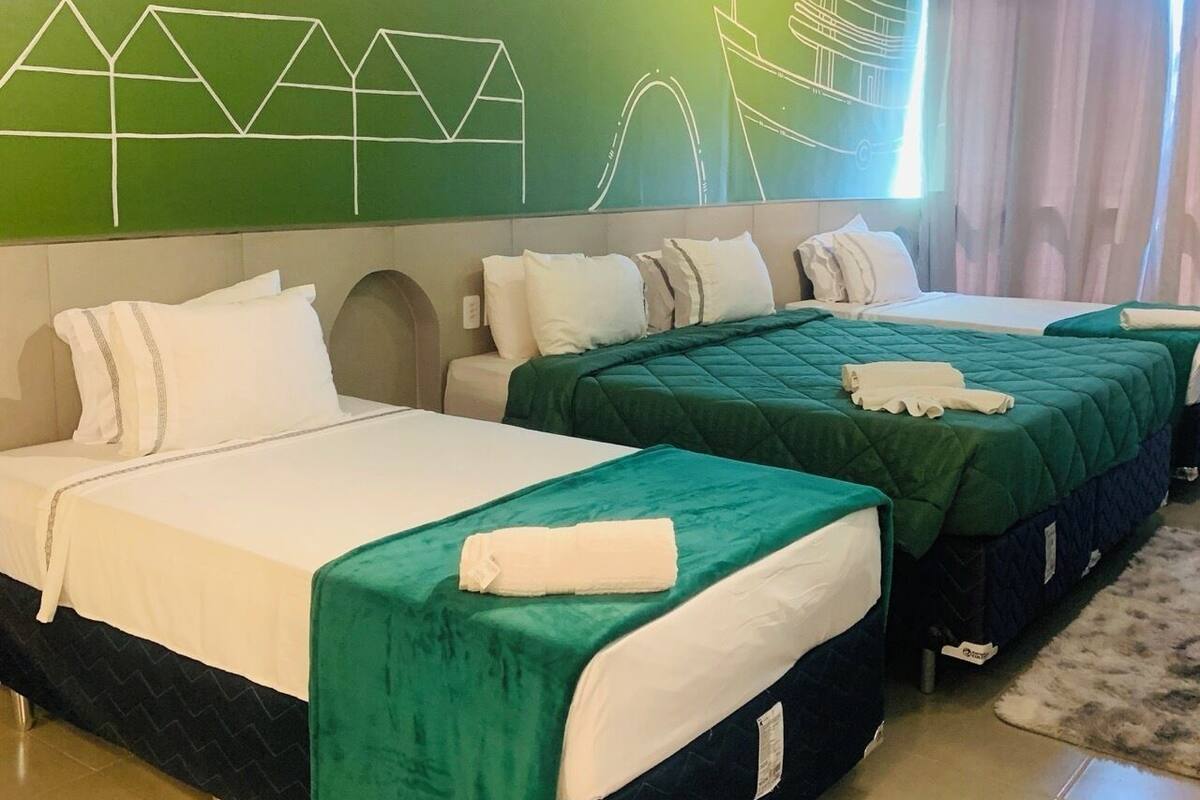 A hotel room with two beds, a green wall with white abstract designs, and a window with curtains.