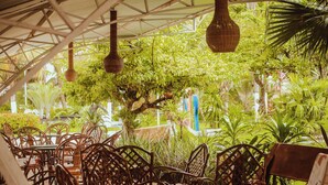 An outdoor seating area with wicker chairs and tables, surrounded by lush greenery and hanging wicker lamps. - Barrudada Tropical Hotel (Santarém)