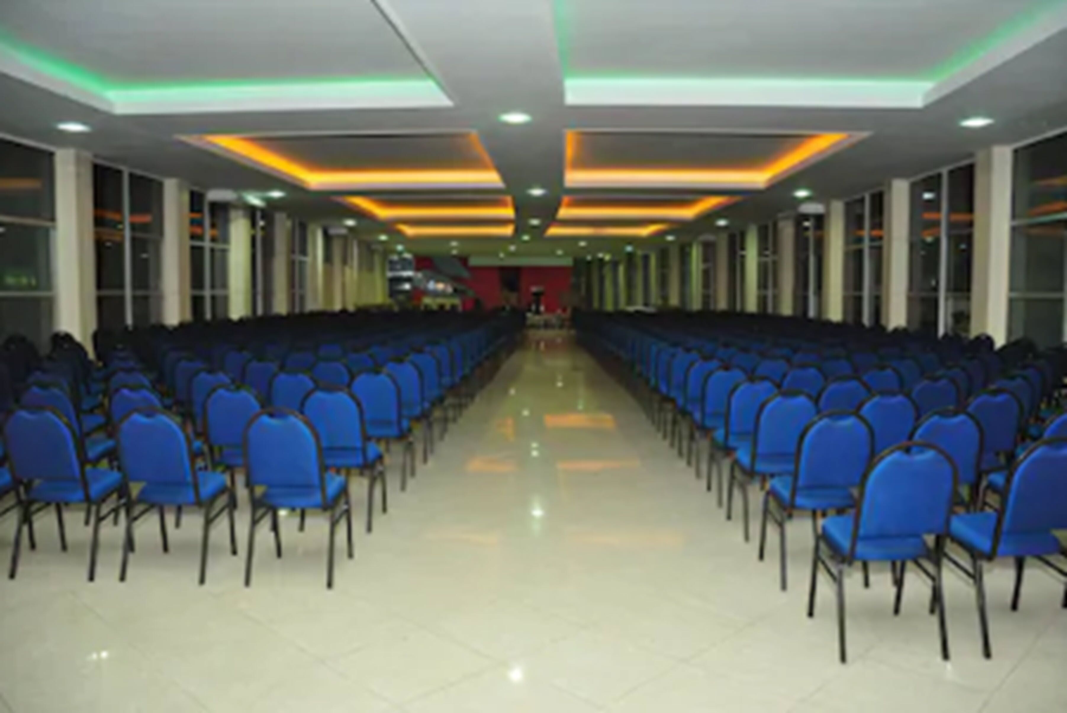 Un salón de conferencias con filas de sillas azules, piso pulido e iluminación empotrada en el techo.