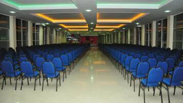 Un salón de conferencias con filas de sillas azules, piso pulido e iluminación empotrada en el techo.