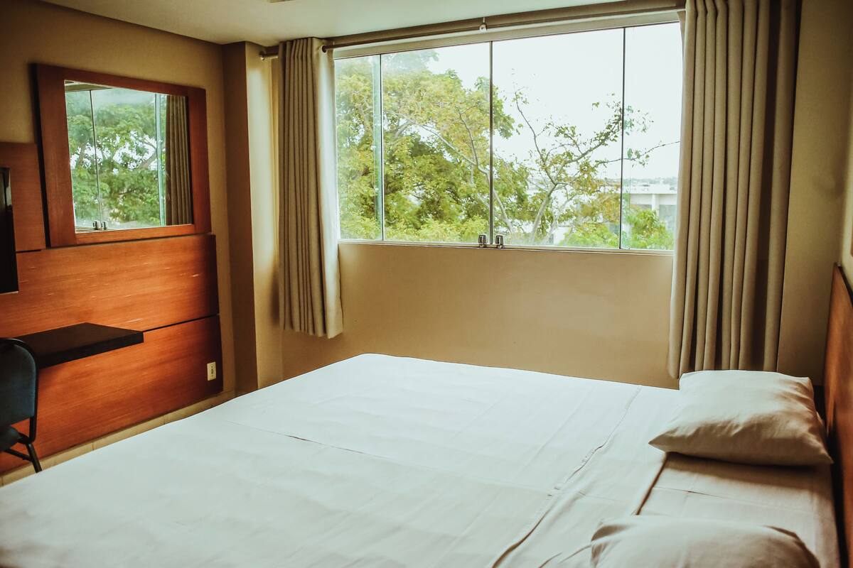 A hotel room with a bed, a desk, and a window with curtains.