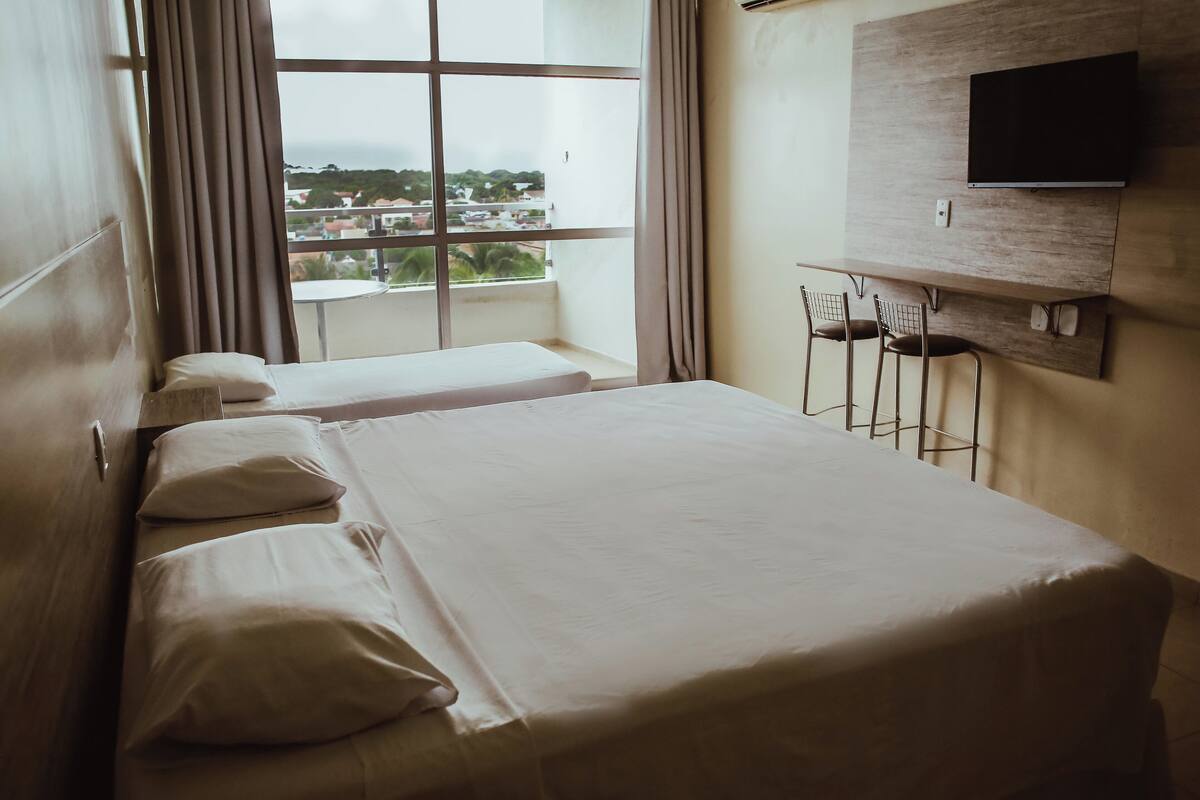 A hotel room with a large bed, a TV mounted on the wall, and a window with a view of the city.