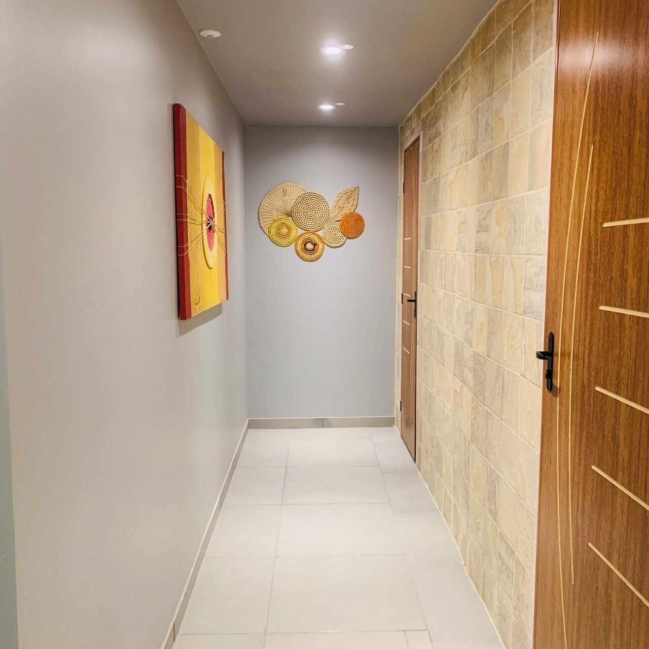 A hallway with a tiled floor, a wooden door, and a wall with decorative wall art.