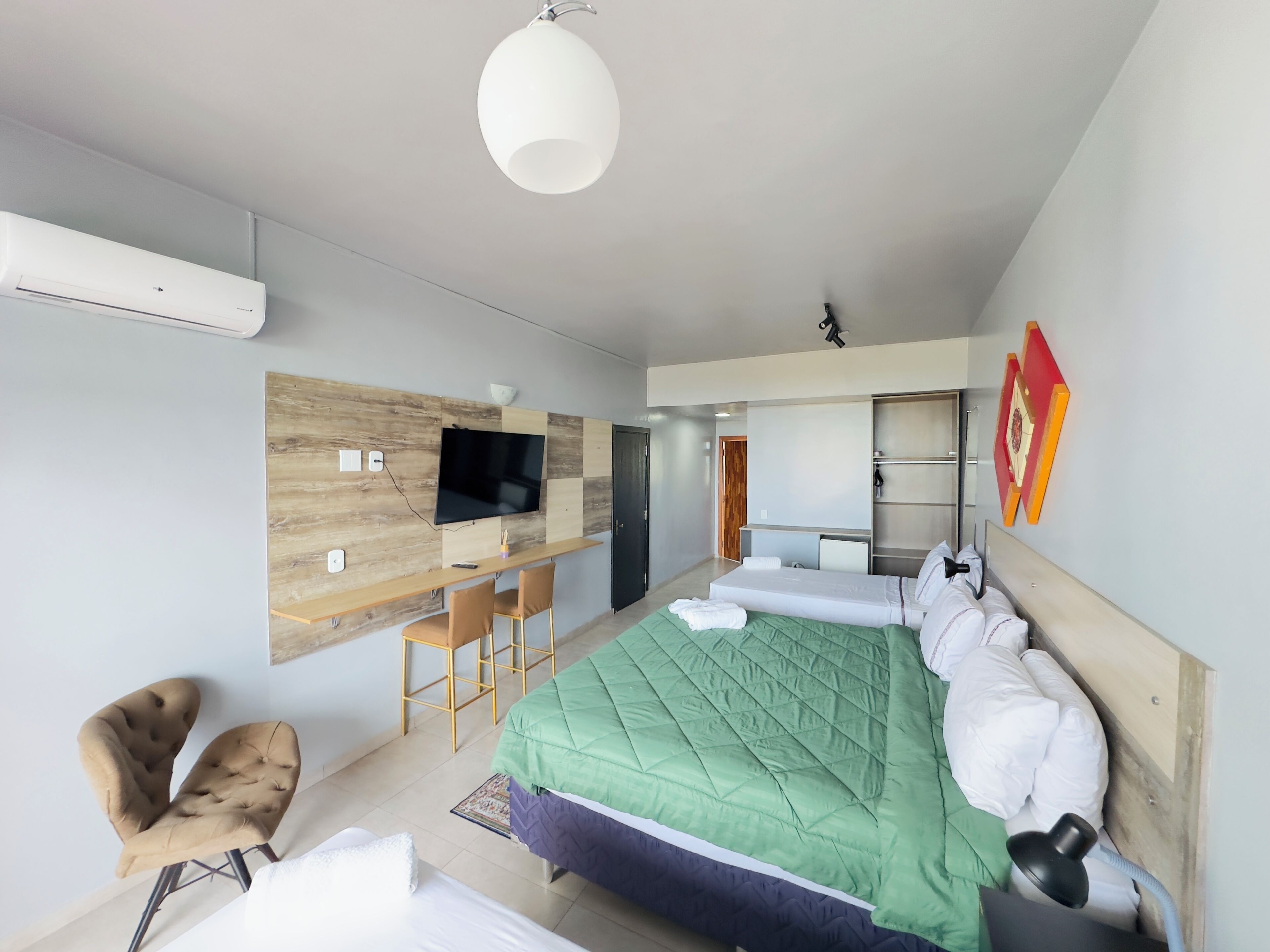 A modern hotel room with a large bed, a desk with chairs, a flat-screen TV, and a wooden accent wall.