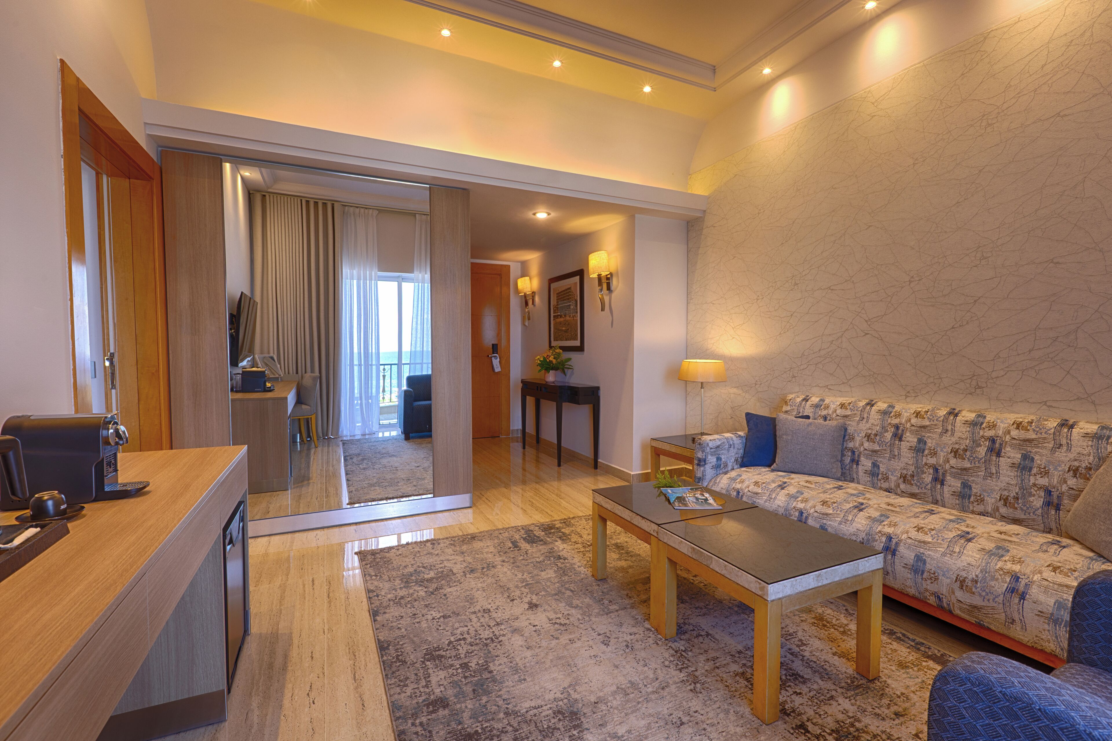 Una habitación de hotel moderna con sofá, una mesa de centro y un escritorio con cafetera.