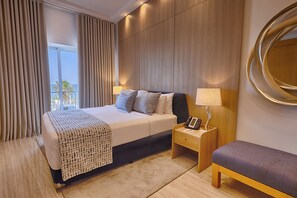 A hotel room with a bed, bedside tables, a lamp, a mirror, and a view of the outdoors.