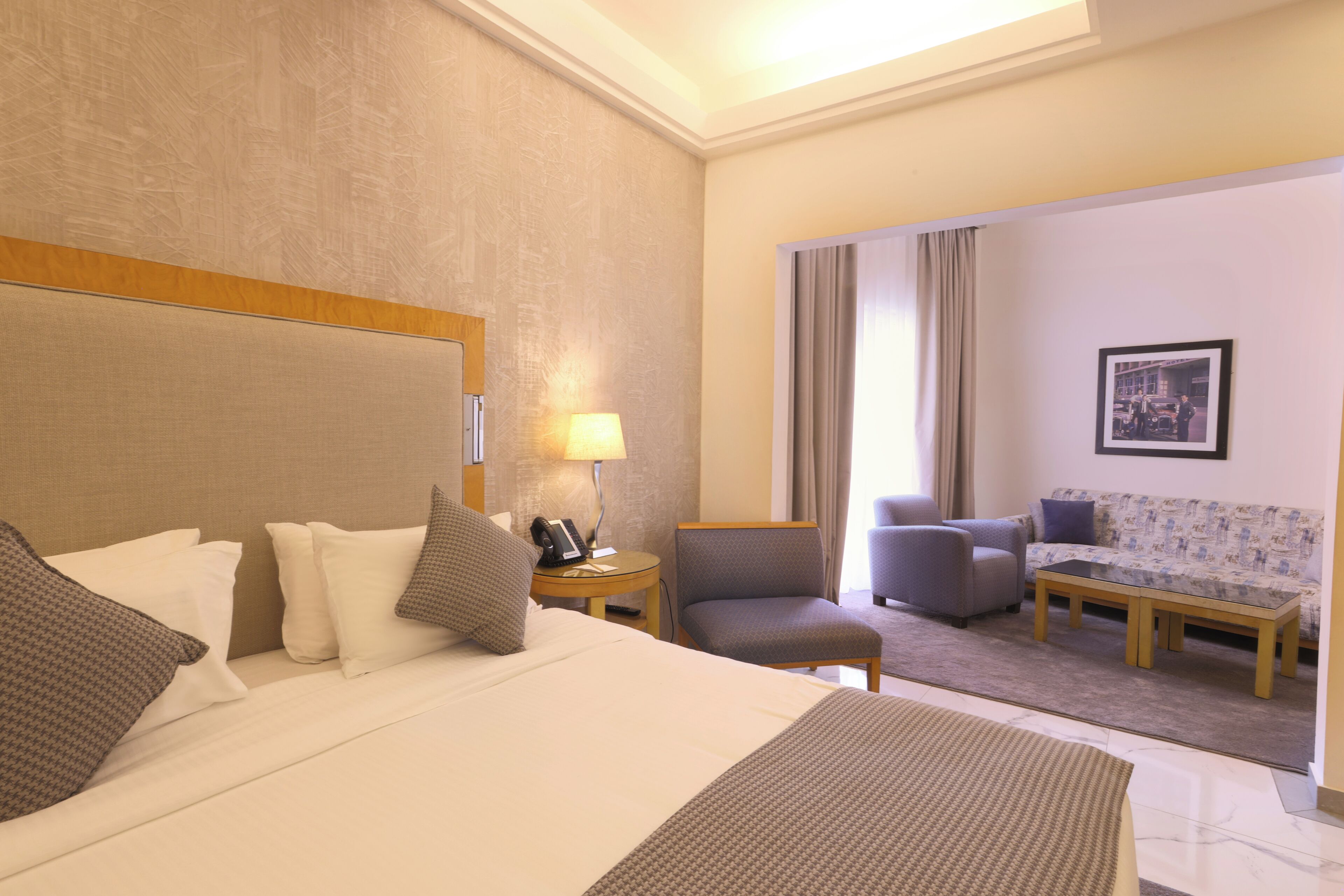 Una habitación de hotel con cama, escritorio, silla, sofá y ventana con cortinas.
