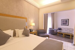 Quarto de hotel com cama, escrivaninha, cadeira, sofá e janela com cortinas.