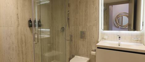 A modern bathroom with a glass-enclosed shower, a white toilet, and a vanity with a mirror.