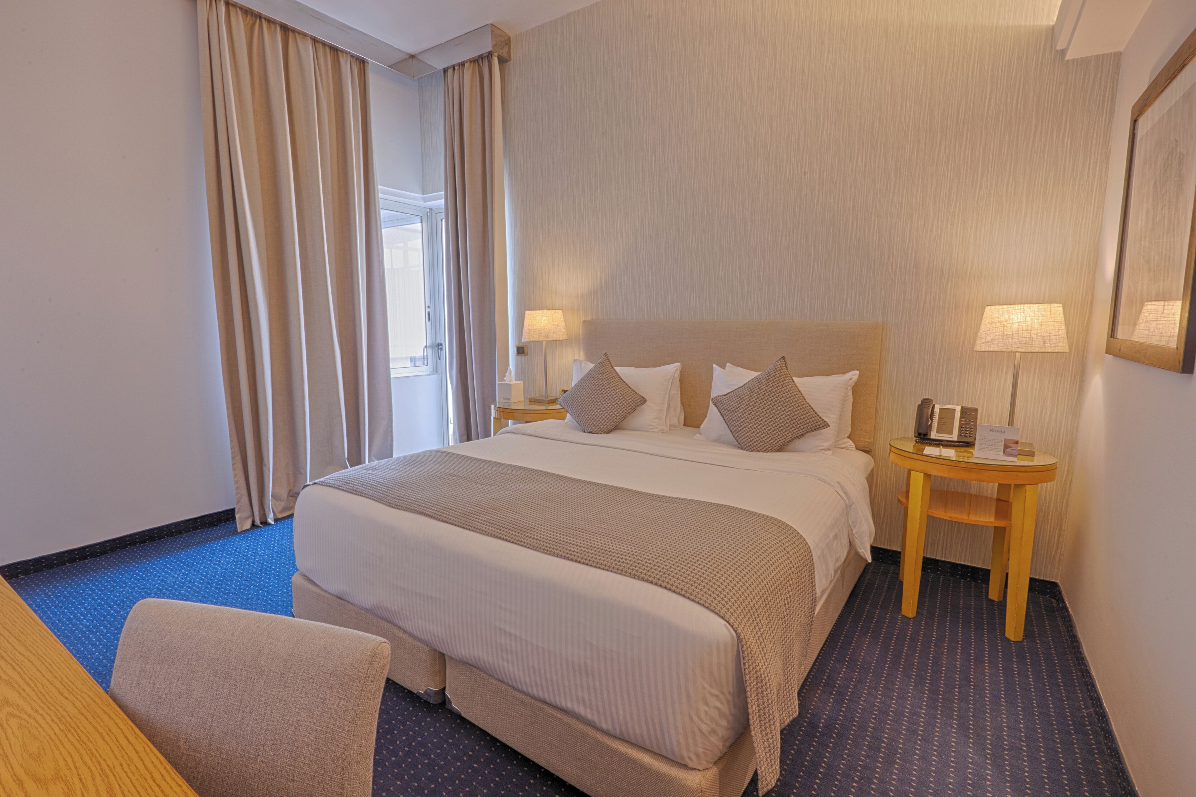 A hotel room with a large bed, two bedside tables, a chair, and a window with curtains.