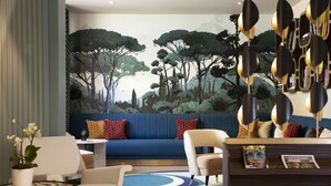 A modern living room with a blue sofa, white chairs, a coffee table, and a decorative plant. - Hotel Aiglon (Paris)