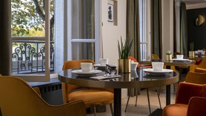 A dining area with round tables, chairs, and a view of the outdoors. - Hotel Aiglon (Paris)