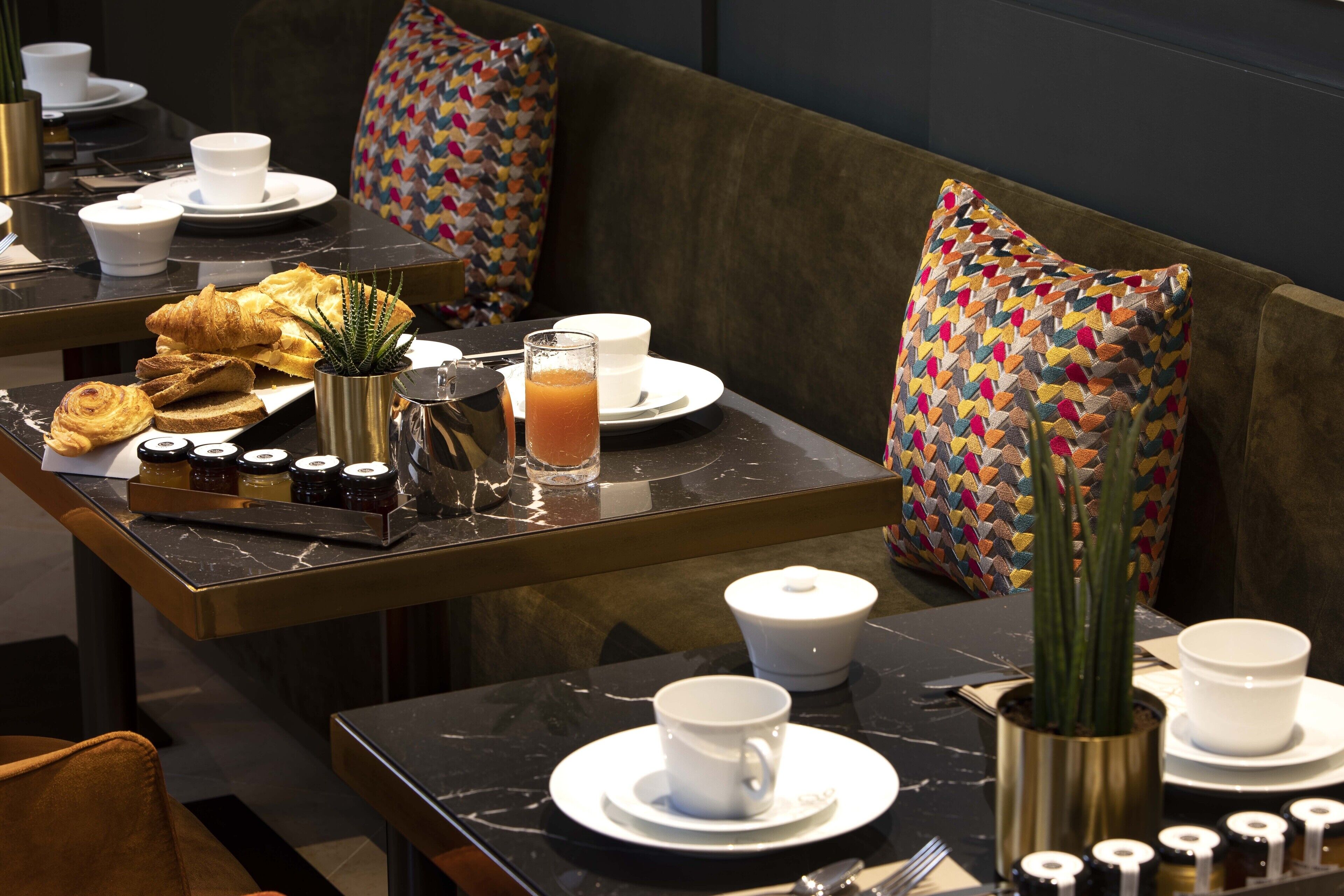 A dining area with a table set for breakfast, including croissants, a coffee pot, and a glass of orange juice.
