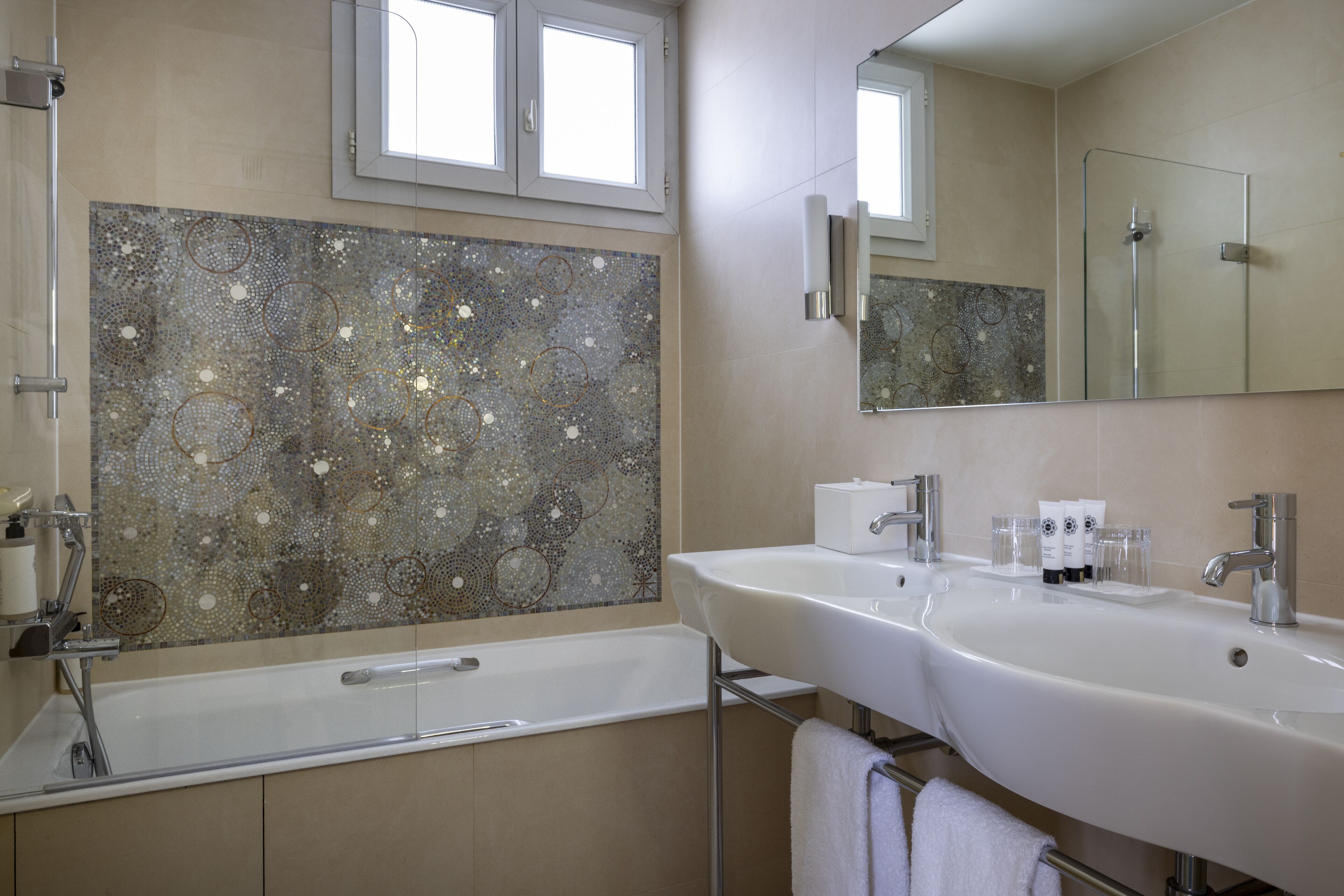 A modern bathroom with two sinks, a large mirror, and a decorative mosaic wall.