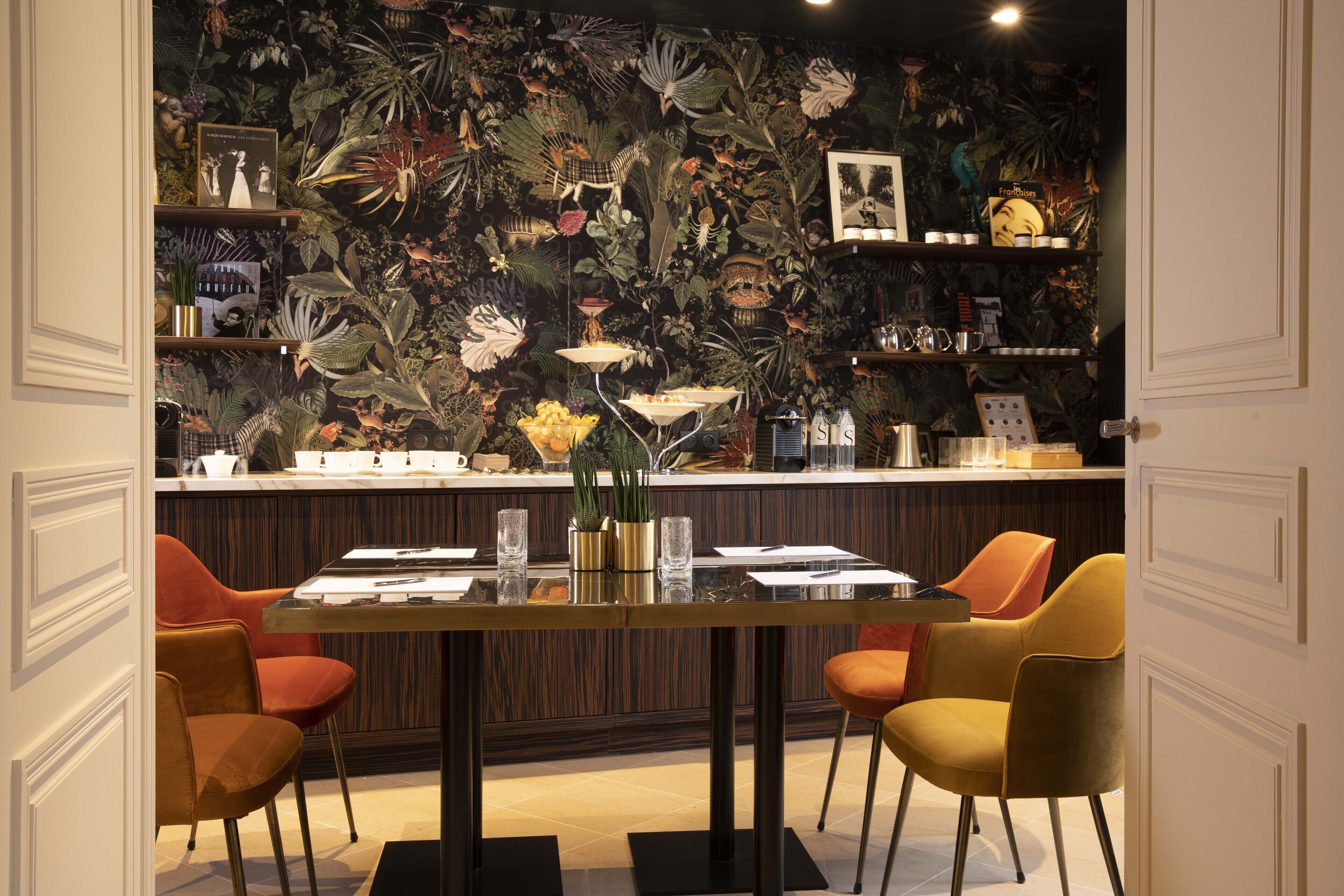 A dining area with a tropical-themed wallpaper, a wooden bar, and orange chairs.