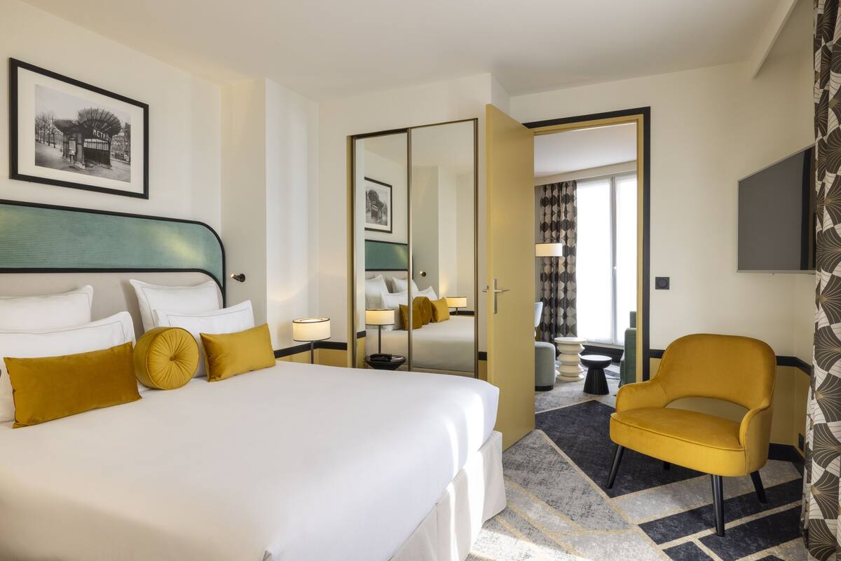 A hotel room with a large bed, a chair, a desk, and a mirror.