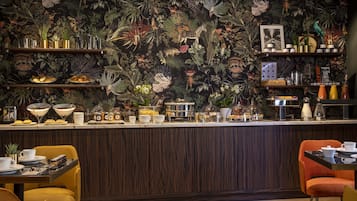 Ein Restaurant mit tropisch gestalteter Wand, einer Holztresen und gelb-orangen Stühlen.