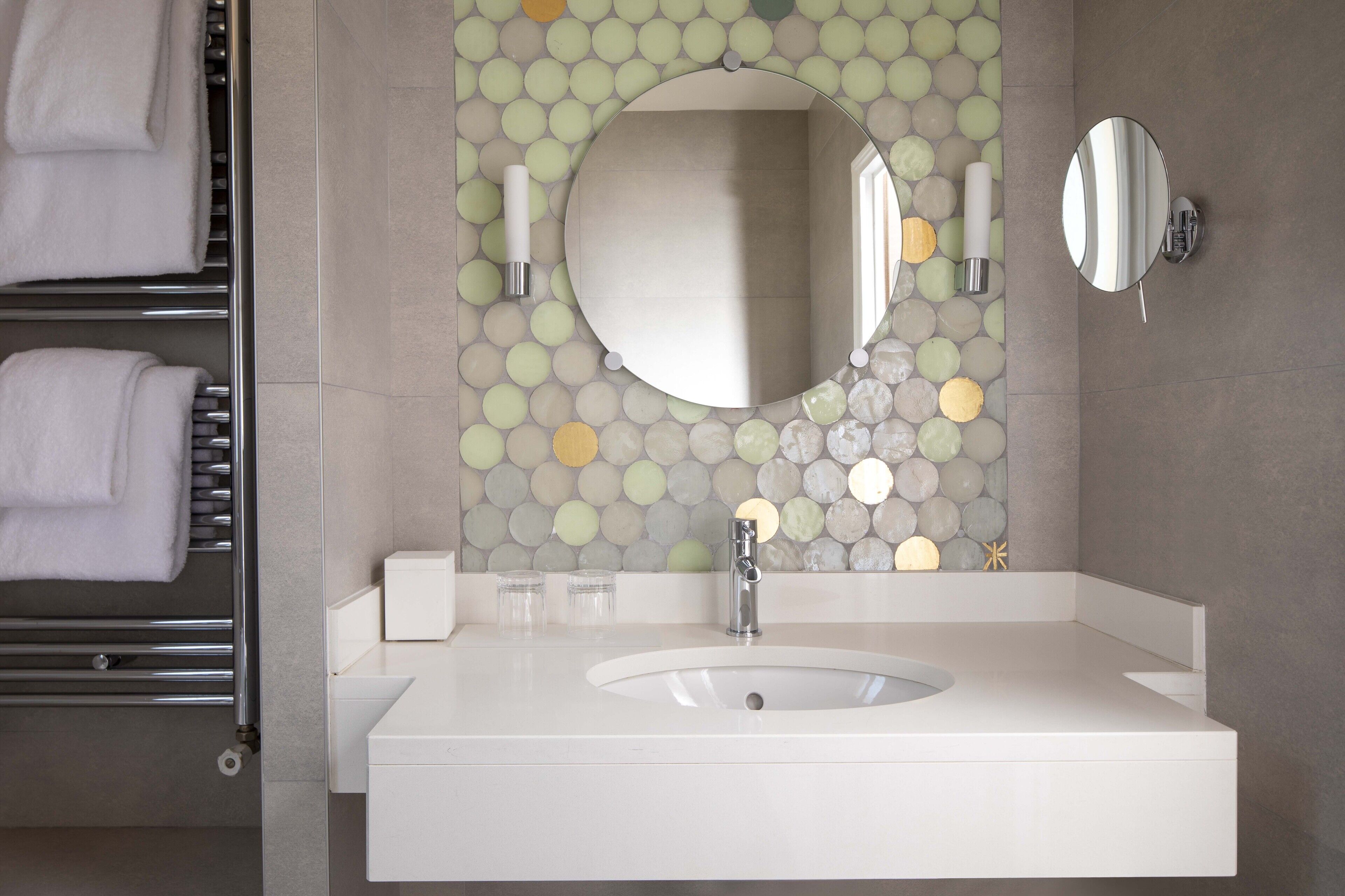 A bathroom with a white sink, a round mirror, and a towel rack with folded towels.