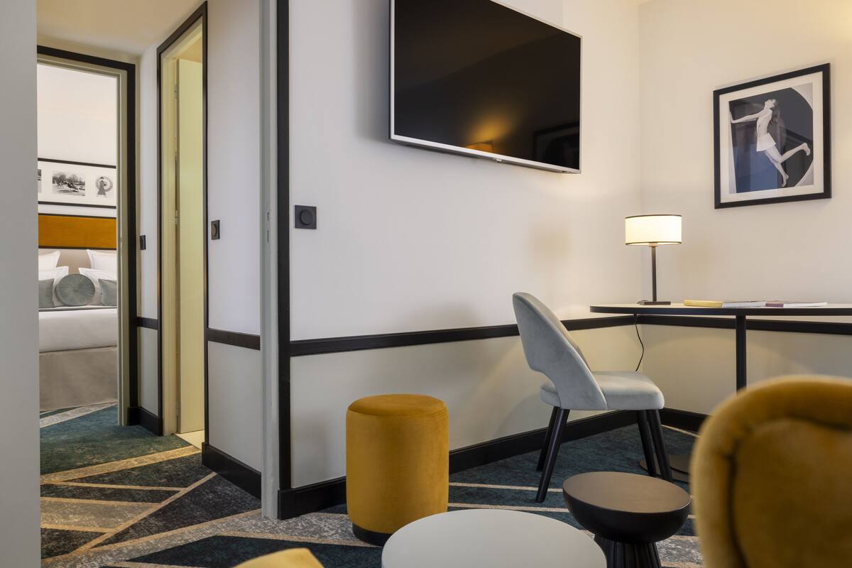 A hotel room with a bed, a desk, a chair, a lamp, and a television.