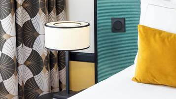 A neatly arranged hotel room with a bed, a bedside lamp, and a curtain with a geometric pattern.