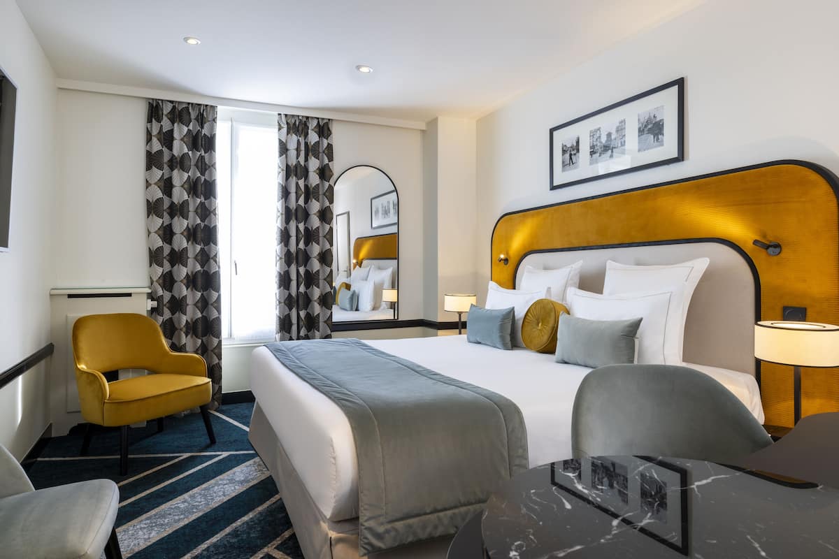 A hotel room with a large bed, two armchairs, a desk, and a mirror.