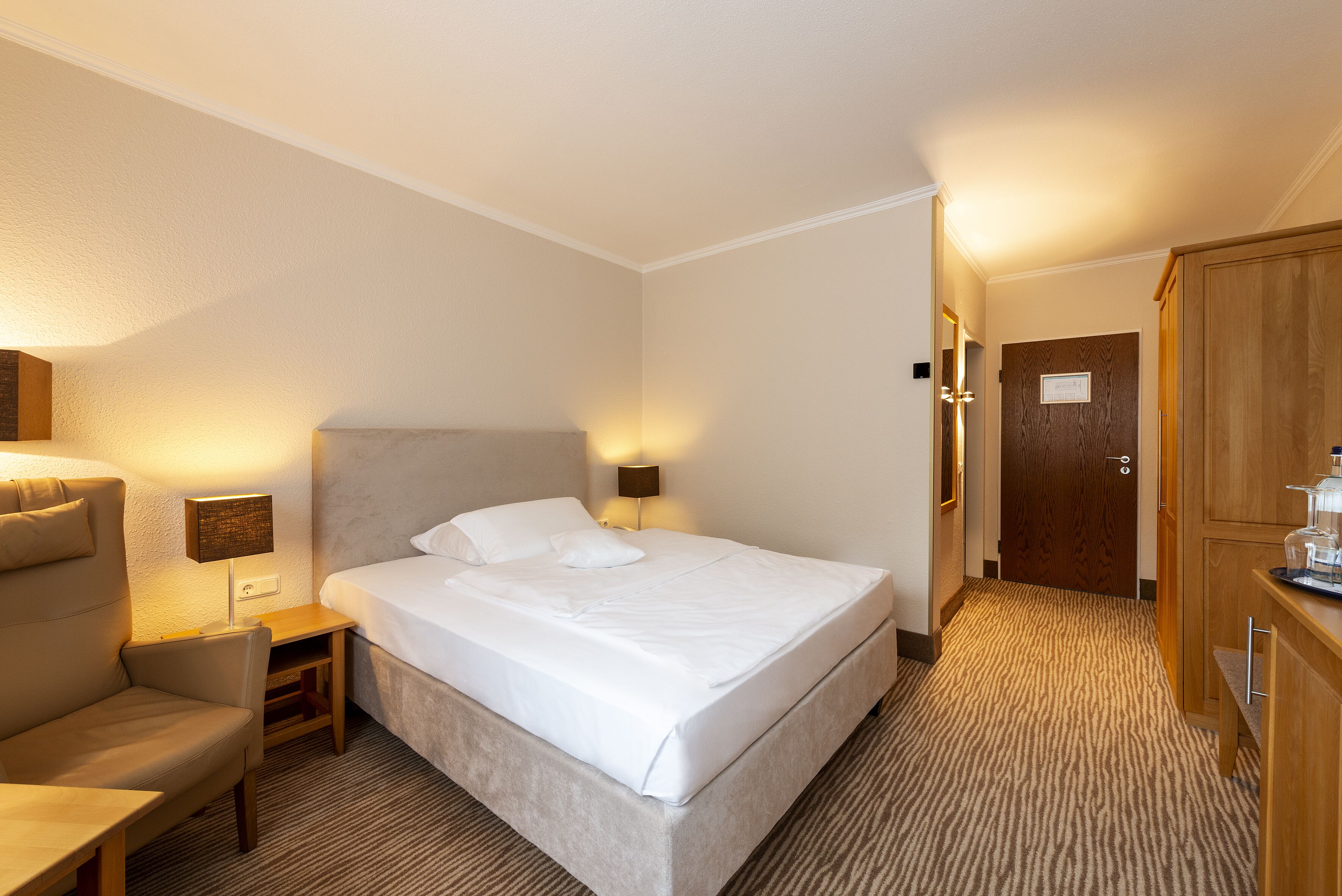 Une chambre d’hôtel comprenant un lit, une chaise, un bureau, une lampe et une armoire.