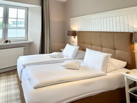 A hotel room with two beds, a window with blinds, a radiator, and a nightstand with a lamp.